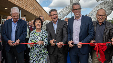 Ministerpräsident Rhein (Mitte) mit weiteren Beteiligten bei der Eröffnung des Bildungs- und Sportcampus. Sie stehen nebeneinander vor einem roten, mit Schleife gebundenen Band und schneiden mit Scheren das Band durch.