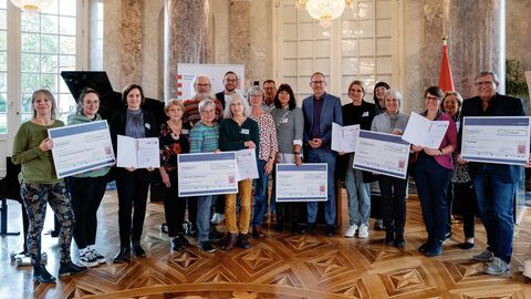 Sozialminister Klose mit einer Gruppe von Preisträgerinnen und Preisträgern. Sie halten Gewinnschecks in den Händen und sind zum Gruppenbild aufgestellt.