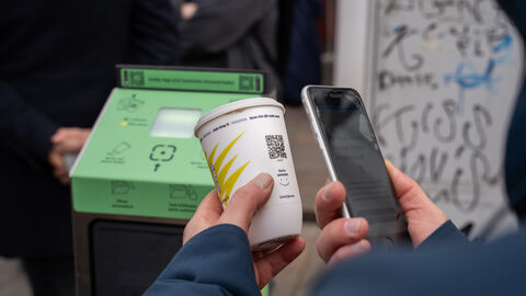 Person scannt mit Smartphone den QR-Code eines Bechers