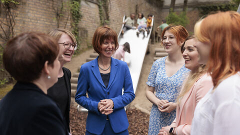 Sozialministerin Hofmann inmitten einer Gruppe Frauen. Im Hintergrund spielen Kinder auf einer Rutsche.