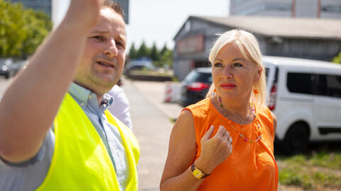 Digitalministerin Sinemus steht mit einem Mann in gelber Weste auf einem Gelände.