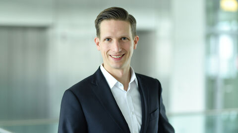 Ein Mann trägt einen Anzug und ist ab dem Oberkörper zu sehen.