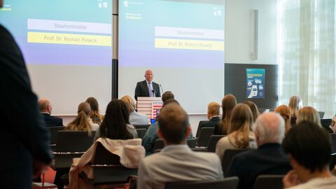 Roman Poseck steht an einem Pult und hält vor einem Publikum eine Rede.