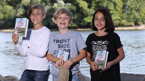 Drei Kinder mit dem Comicroman „Iva, Samo und der geheime Hexensee“ zum Welttag des Buches 2022.
