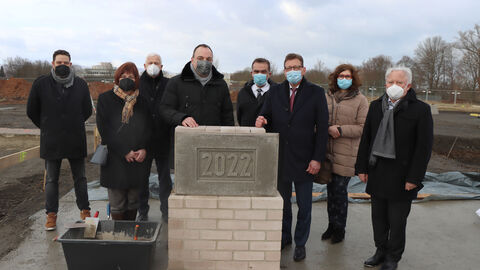 Grundsteinlegung für den Neubau des Polizeireviers Ost in Kassel. Um den Grundstein sind der Staatssekretär des Hessischen Ministeriums des Innern und Sport Stefan Sauer, Ortsbürgermeister Christian Geselle, der nordhessische Polizeipräsident Konrad Stelzenbach und weitere Vertreterinnen und Vertreter aus der Bauverwaltung und Polizei versammelt.