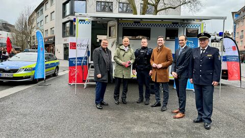Oberbürgermeister Frank-Tilo Becher, Innenminister Roman Poseck, Ordnungspolizist Lars Wiegandt, Landtagsabgeordneter Frederik Bouffier, Polizeipräsident Torsten Krückemeier und der stellv. Leiter der Polizeidirektion Gießen Rene Kopsch stehen gemeinsam in der Innenstadt vor einem Werbestand.
