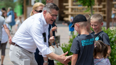 Ministerpräsident Rhein mit drei schüttelt die Hand eines Jungen, nebendran weitere Kinder.