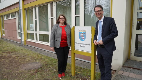 Eine Frau und ein Mann stehen jeweils neben einem Gebäudeschild mit der Aufschrift "Verwaltungsgericht Gießen"
