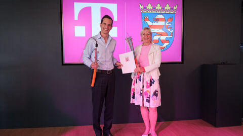 Herr Rodrigo Francisco Diehl, Vorstand Deutschland und Sprecher der Geschäftsführung der Telekom Deutschland und Hessens Digitalministerin Prof. Dr. Kristina Sinemus stehen zusammen vor einem Bildschirm mit dem Telekom-Logo und dem Wappen Hessens.