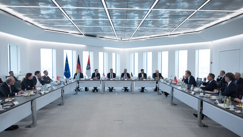 In einem Hochhaus stehen Tische in einer U-Form, wo Menschen dran sitzen.